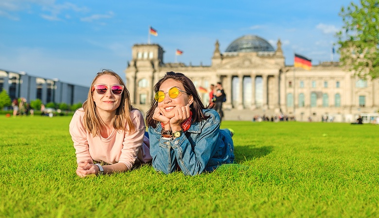 Two young happy girls wearing sun glasses lying on a grass in front of the Bundestag building in Berlin