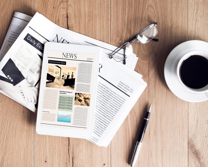 News on a tablet, on top of a newspaper on a wooden desk